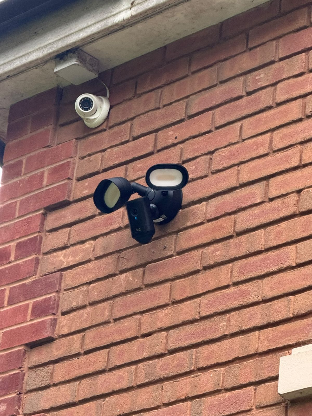 Security floodlight camera and CCTV mounted on brickwork